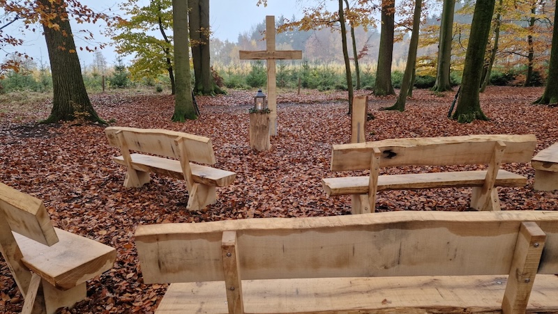 Kleiner Andachtsplatz im herbstlichen Wald mit Holzkreuz und einfachen Holzbänken.